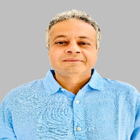 A man with short gray hair wearing a light blue button-up shirt against a gray background.