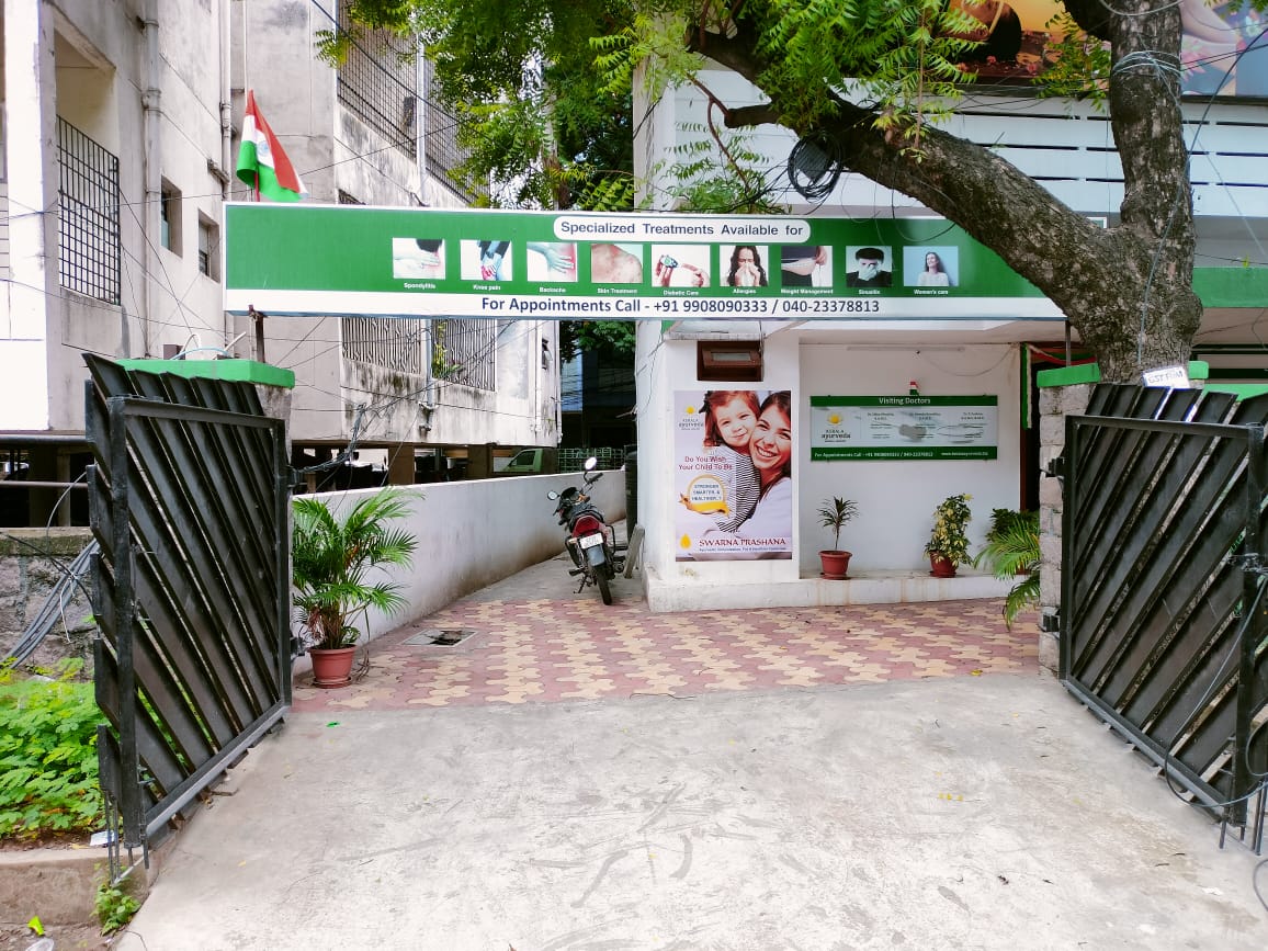 Entrance of a clinic with a motorcycle parked, surrounded by plants and featuring a promotional poster.