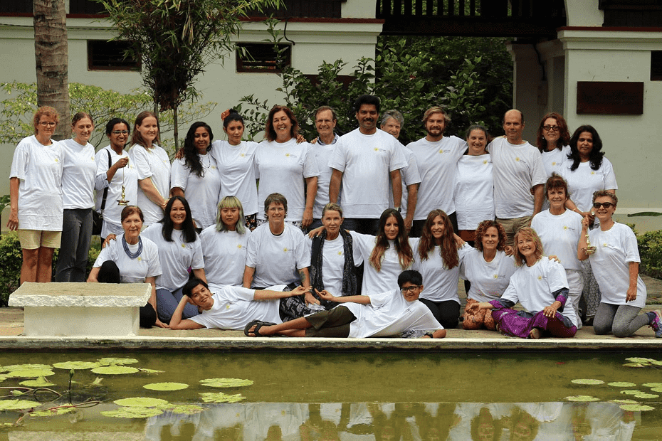 Group photo of people in white t-shirts gathered outdoors near a pond with lily pads.
