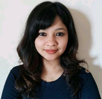 A woman with long dark hair and a blue top is smiling against a light background.