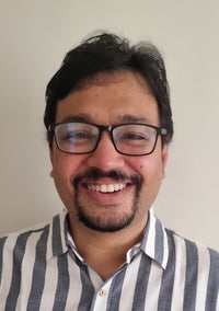 Smiling man wearing glasses and a striped shirt against a plain background.