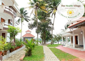 A view of The Health Village with buildings, palm trees, and a pathway near a water body.