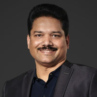 A man in a black suit smiles against a dark background.