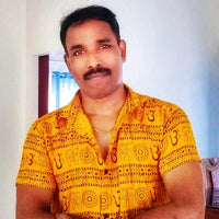 A man in a yellow patterned shirt poses with his arms crossed in a well-lit indoor setting.