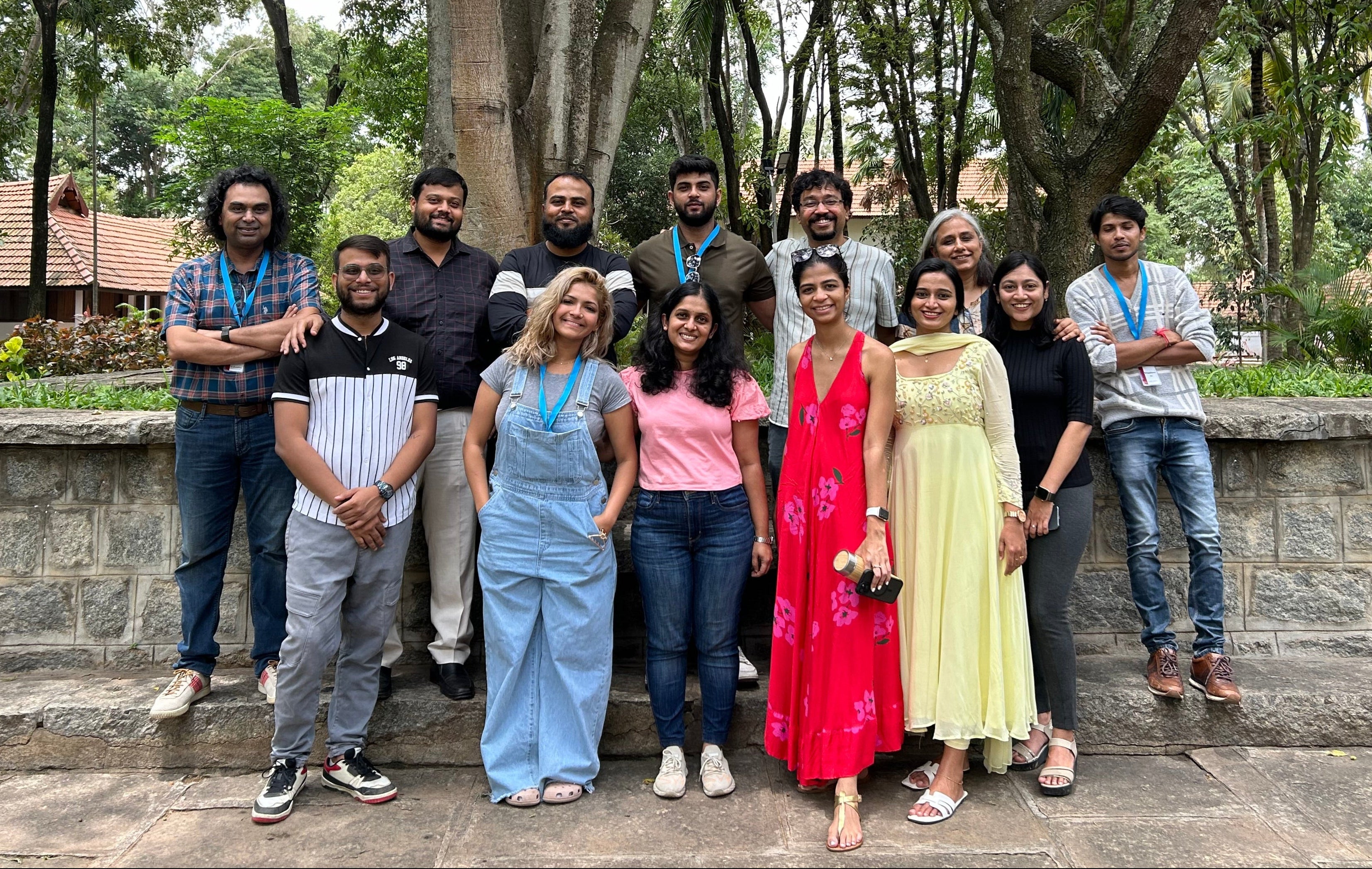 Group photo of diverse individuals posing outdoors in a park setting, smiling and standing on a stone pathway.