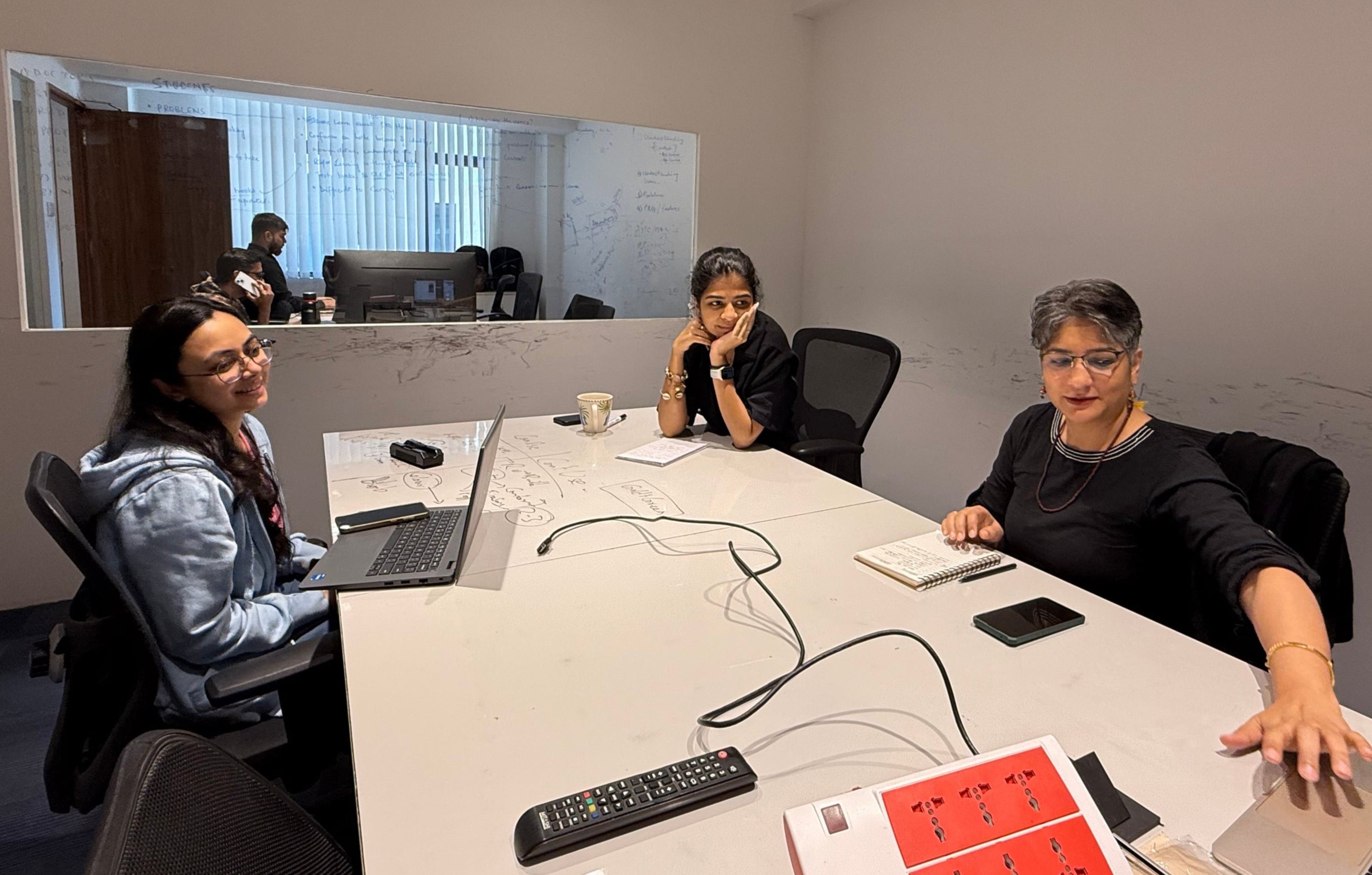 Three people engaged in a discussion around a conference table in a modern office setting.