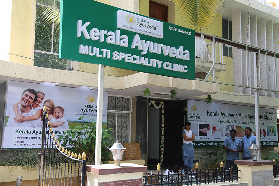 A multi-specialty clinic building with signs for Kerala Ayurveda and family images on banners.