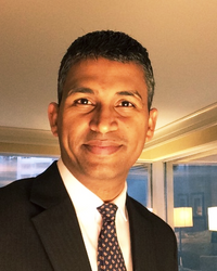 A man in a suit and tie smiles in a well-lit indoor setting.