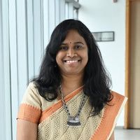 A woman in a traditional saree smiles while standing in a corridor.