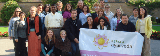 A diverse group of people posing together outdoors, holding a banner for Kerala Ayurveda.