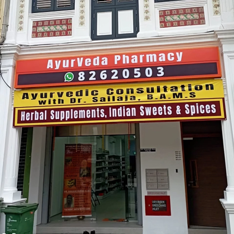 Ayurveda Pharmacy storefront with signs for Ayurvedic consultation and herbal supplements, Indian sweets, and spices.