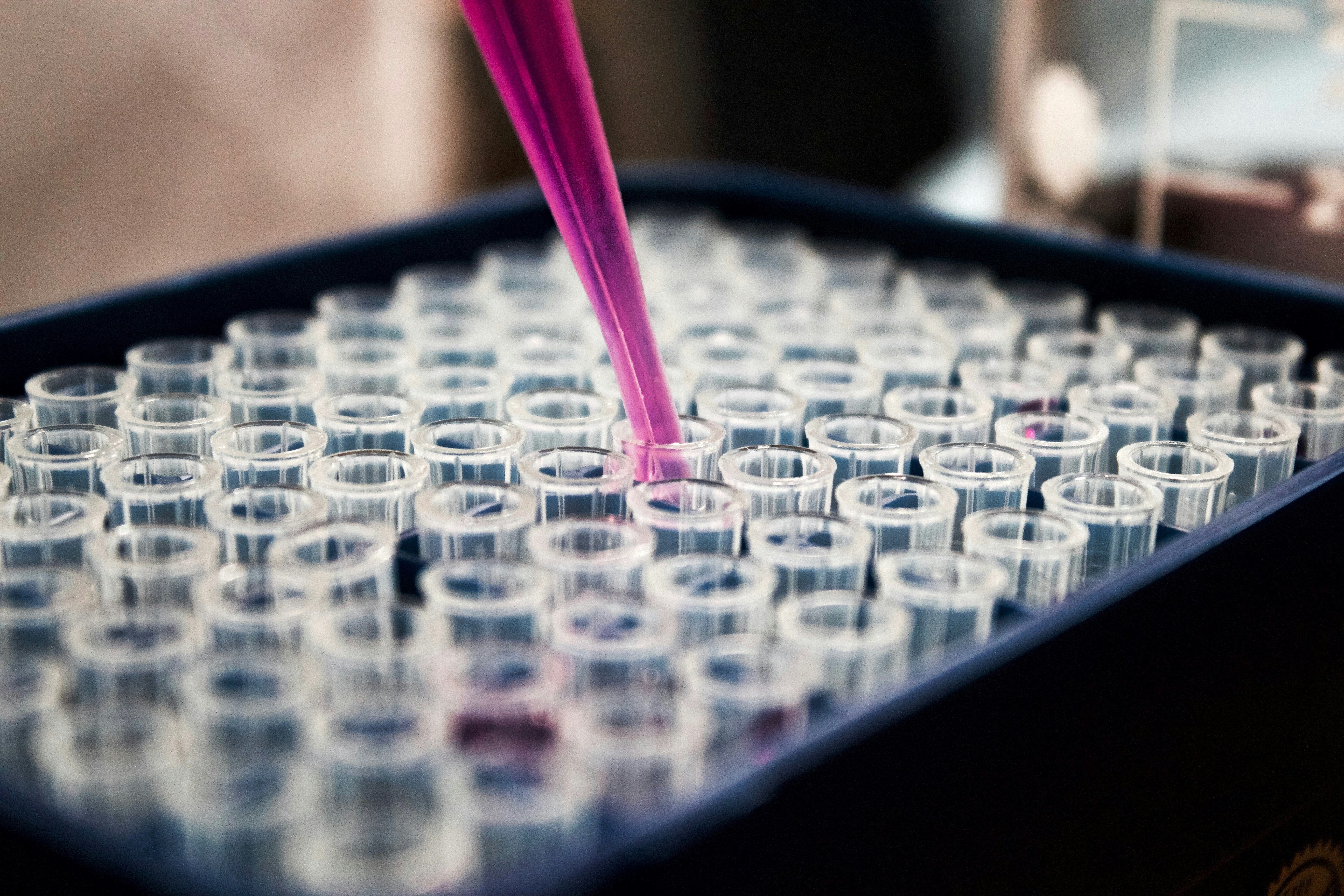 A pipette dispensing liquid into a tray filled with multiple test tubes.