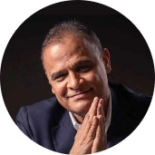 A man in a suit is smiling and posing with his hands clasped together.