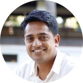 Smiling man with short black hair, wearing a light-colored shirt, posed outdoors in a circular frame.